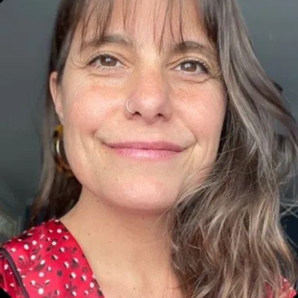Smiling woman with brown hair wearing a red patterned top.
