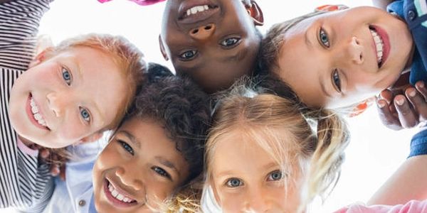 A group of diverse children smiling in a circle looking down.