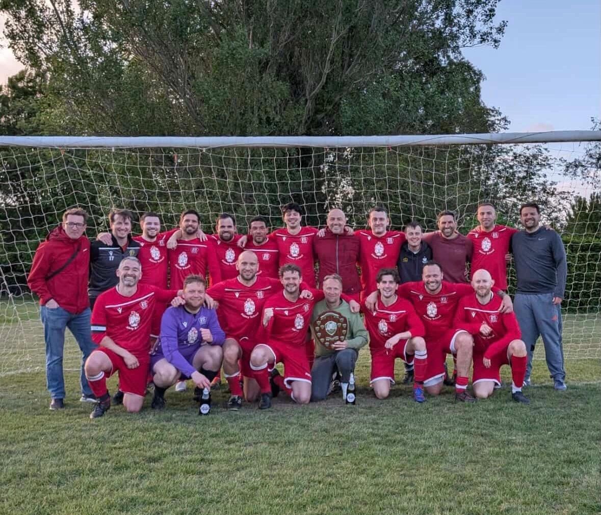 Soccer team posing with a trophy in front of goal net.