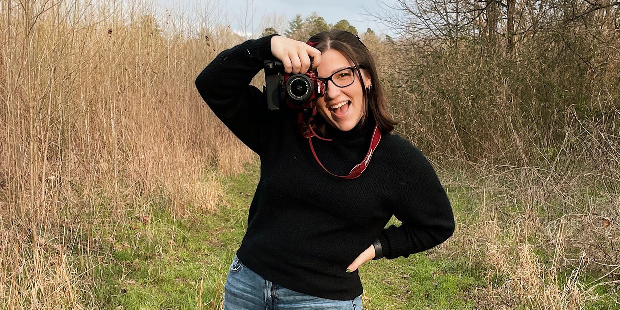 A woman joyfully takes a photo outdoors with a camera on a nature trail.