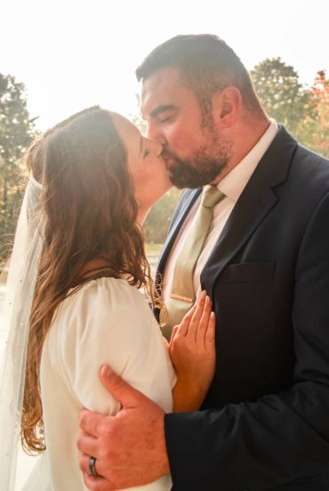 A couple sharing a tender kiss outdoors, dressed formally.