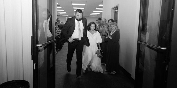 A joyful couple runs down a hallway as guests cheer them on.