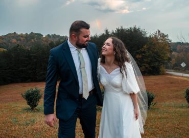 A couple in wedding attire looking happily at each other outdoors.