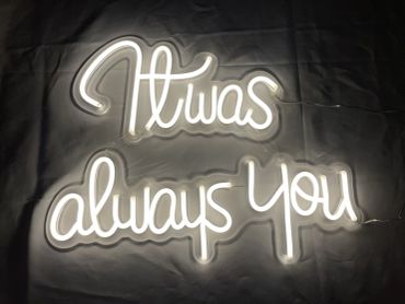Neon sign reading 'It was always you' glowing in the dark.