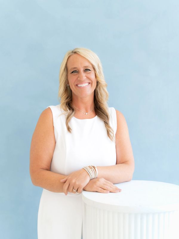 Smiling woman in white dress posing against a light blue background.