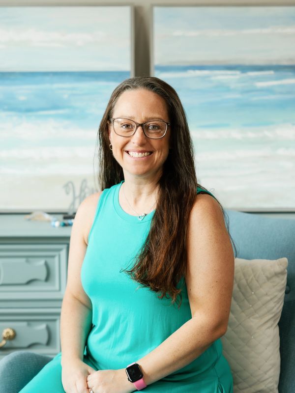 Smiling woman in turquoise dress sitting on a blue chair indoors.