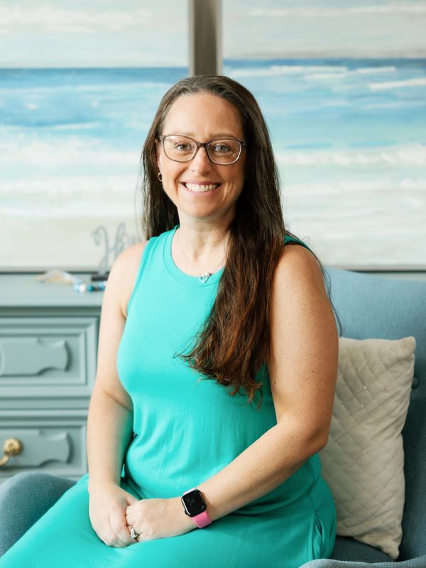 Smiling woman in turquoise dress sitting on a blue chair indoors.