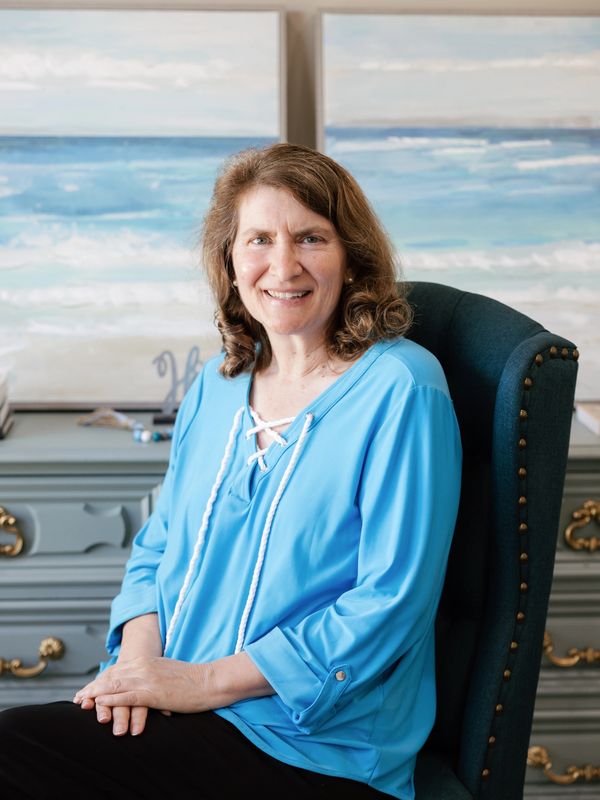 Woman in blue blouse sitting on a chair, smiling.