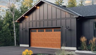 Modern black house with wooden garage door and outdoor lighting.