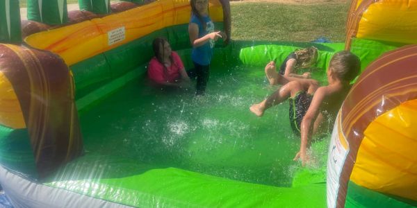 Children playing and splashing in a colorful inflatable pool outdoors.