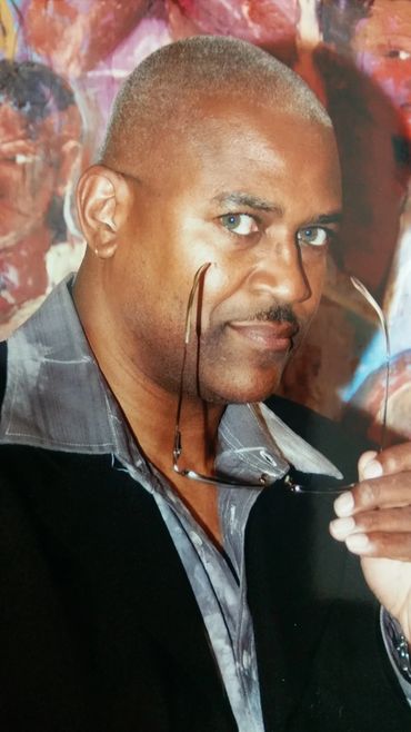 Man with glasses and a confident look, wearing a black jacket and patterned shirt.