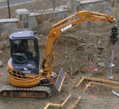 helical pier being installed on a new foundation by a mini excavator