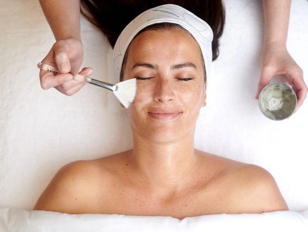 Woman enjoying a facial treatment with a brush applying cream.