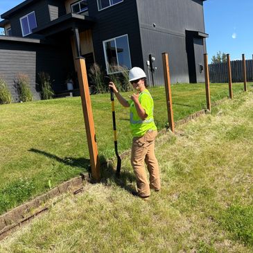 Person in a hard hat working with a shovel near a fence.