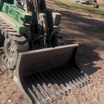 A green skid steer loader with a multi-purpose bucket attachment.