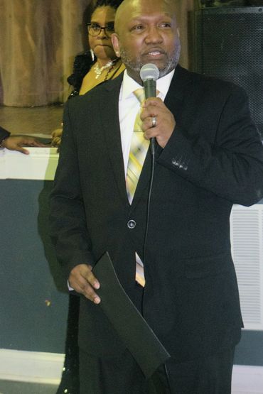 Man in suit speaking into a microphone at an event.