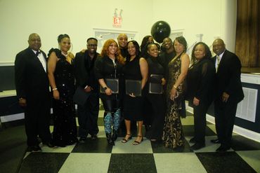 Group of people dressed formally, posing indoors with awards.