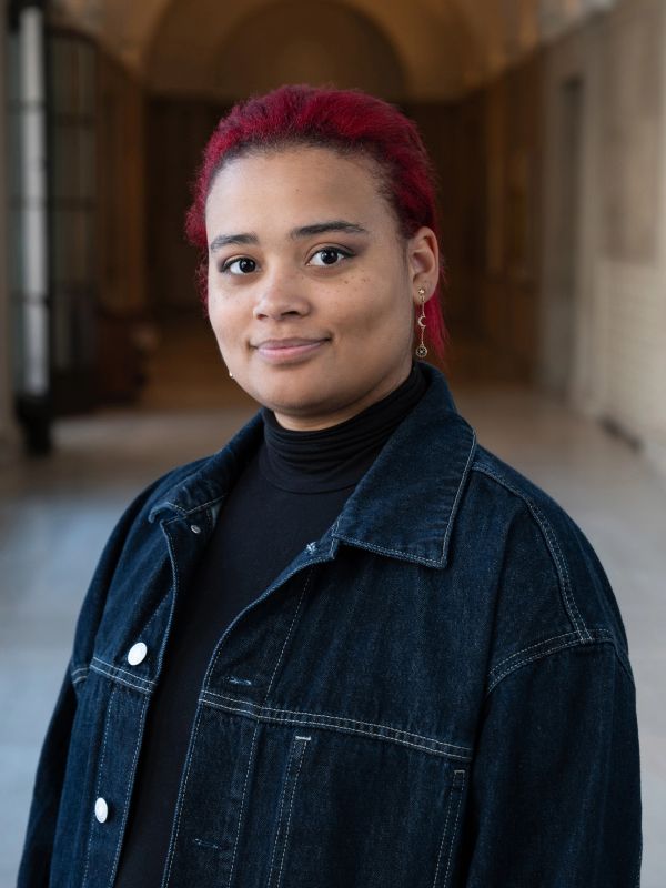 Young person with red hair and denim jacket smiling.