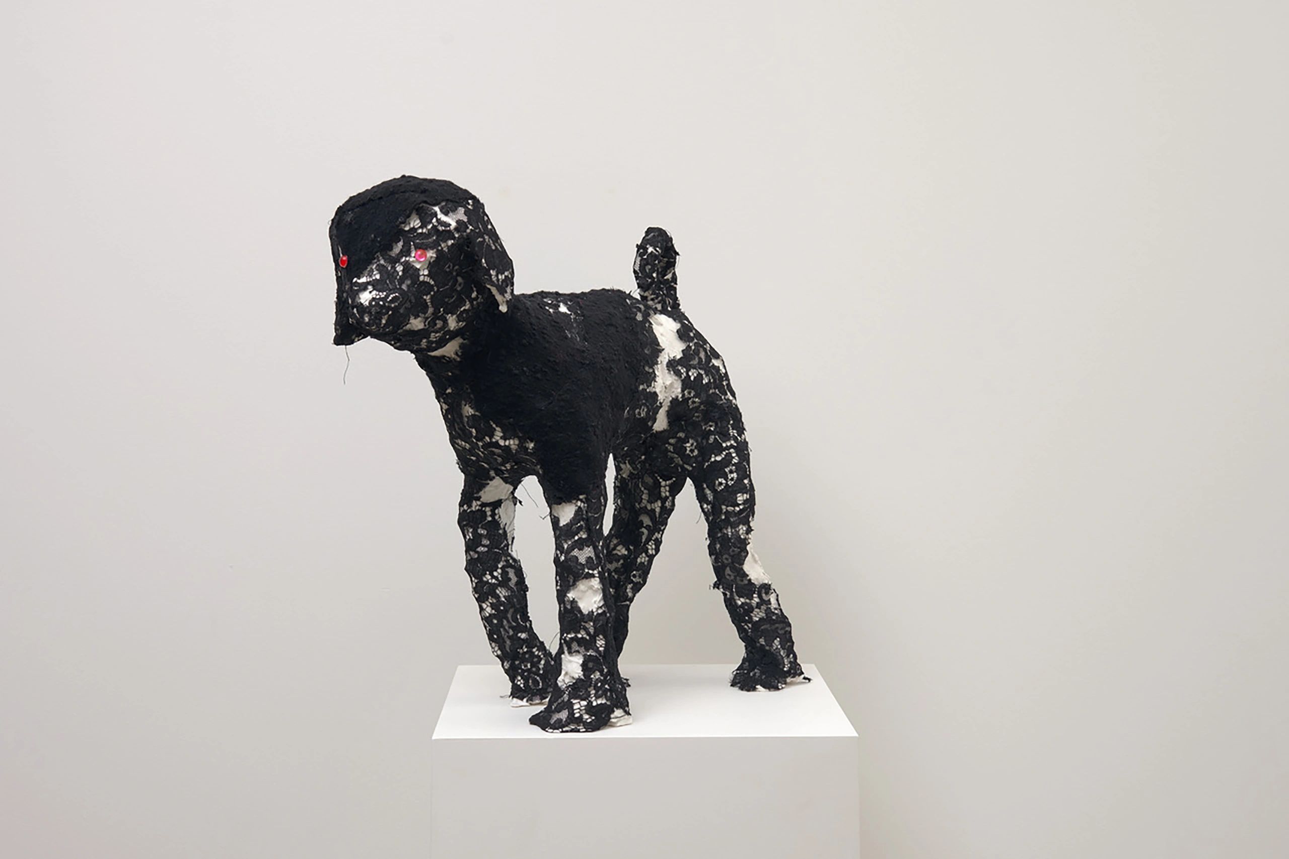 Sculpture of a dog covered in black lace with red eyes on a pedestal.