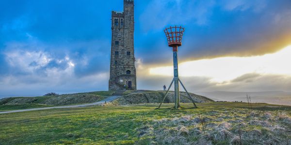 Historic stone tower on a grassy hill under a dramatic sky at sunset.
