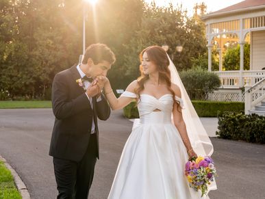 Groom kisses bride's hand during sunset wedding.