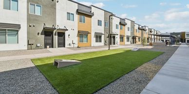 A row of modern townhouses with a shared green lawn and clear sky.