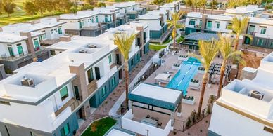 Aerial view of modern white residential villas with a swimming pool and palm trees.