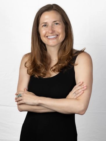 Smiling woman with long brown hair wearing a black sleeveless dress.