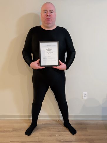 Man in a black bodysuit holding a framed certificate.
