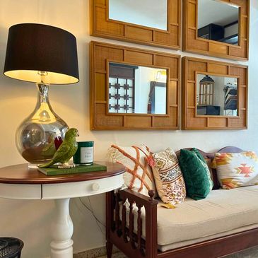 Cozy living room corner with a wooden sofa, colorful cushions, and a decorative lamp on a side table.