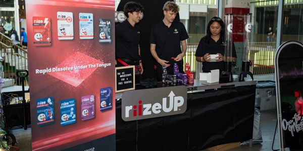 Three people at a rizeUp promotional booth with product display.