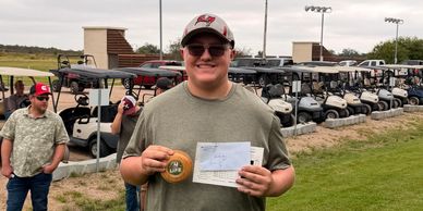 Man holding a check and a disc, standing in front of golf carts.