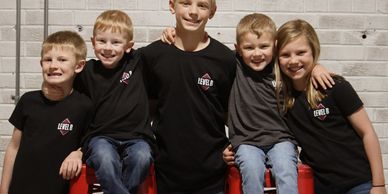 Five children smiling and posing together against a brick wall.