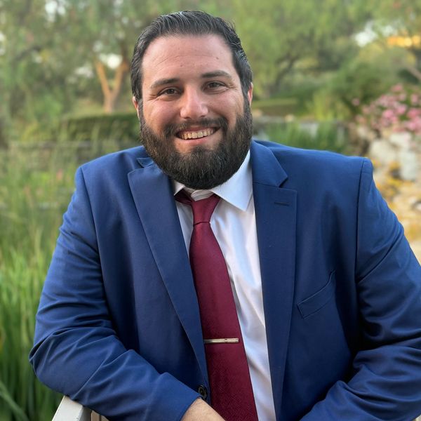 Smiling man in a blue suit and red tie outdoors.