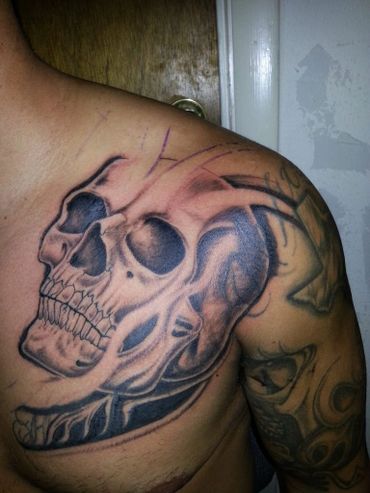 Black and grey tattoo skull on an upper left chest of a man.