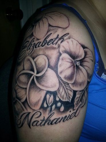 Black and grey flowers tattoo with names, on a shoulder.