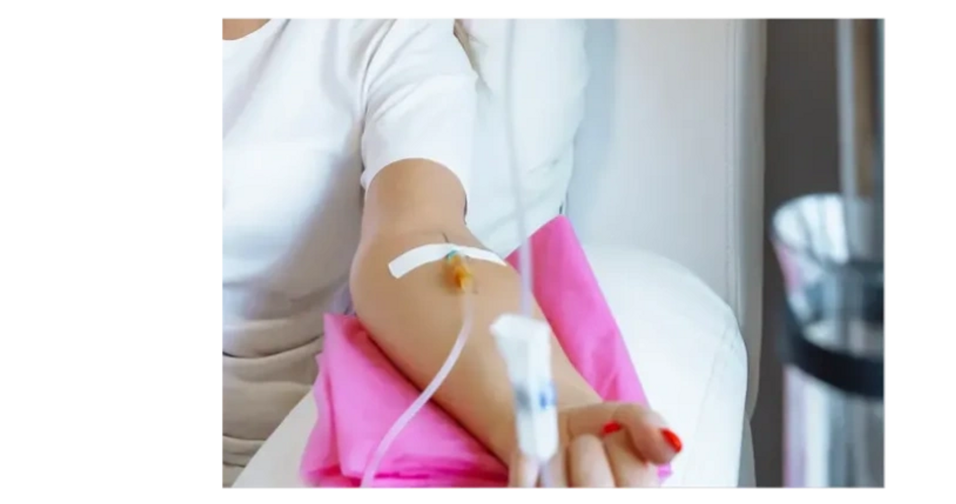 Person receiving intravenous therapy with arm supported by pink cushion.