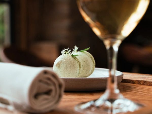 Green macarons on a plate with a glass of wine and a napkin.