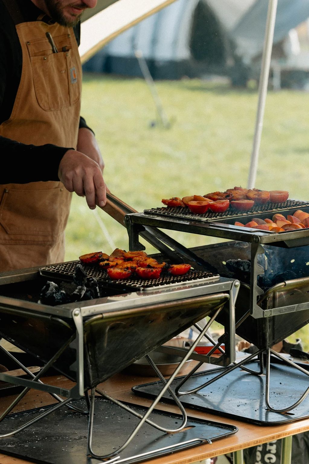 Person grilling vegetables outdoors on portable grills.