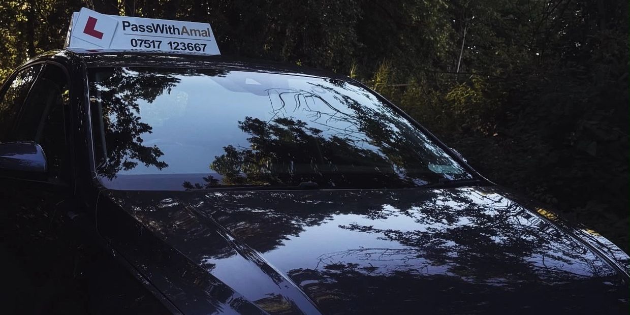 Black car with a learner driver sign on top in a wooded area.