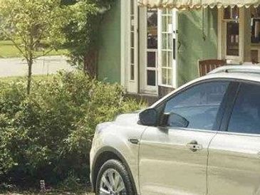 A silver SUV parked outside a green cafe with outdoor picnic tables nearby.