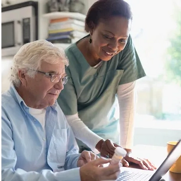 A nurse assists an elderly man with medication using a laptop.