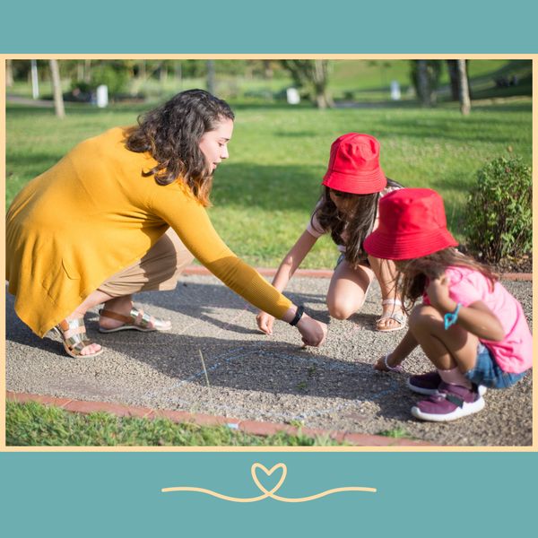 A nanny and two young girls drawing on the ground with chalk.