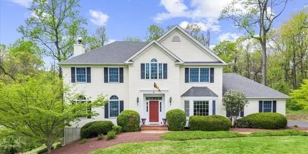 Two-story white house with a red door and green landscaping.