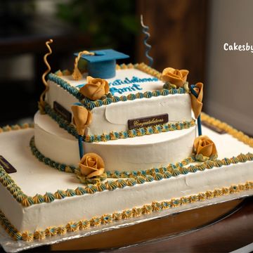 Two-tier graduation cake with golden roses and blue accents.