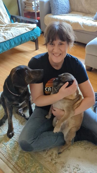 Woman sitting on the floor with two dogs, smiling warmly.