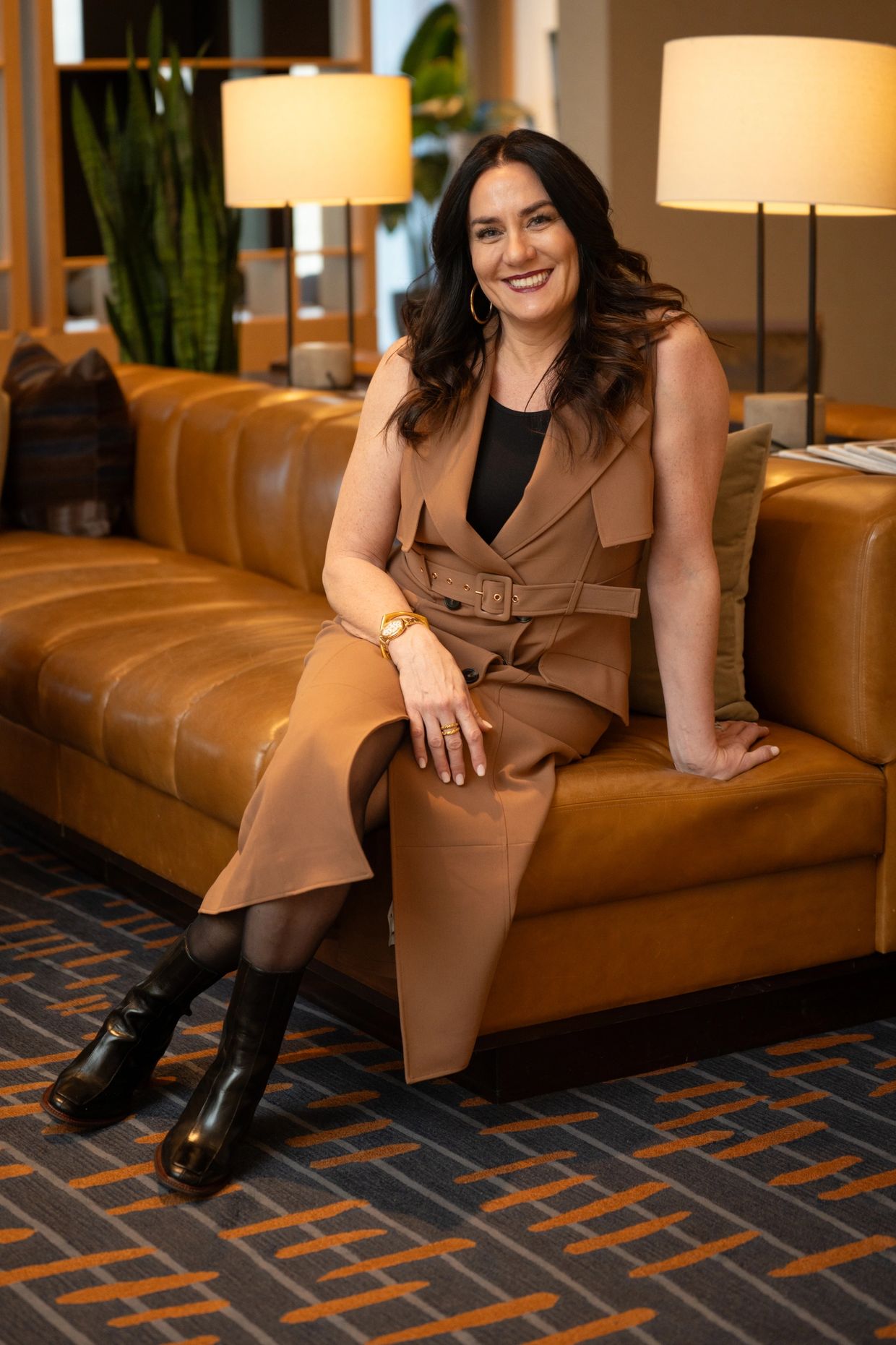 Smiling woman in brown dress sitting on a leather couch in a cozy room.