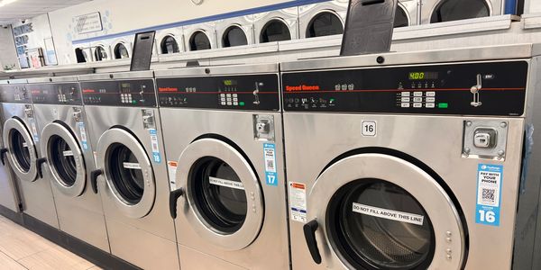 Row of stainless steel commercial laundry machines in a laundromat.