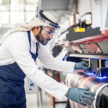 Technician in traditional attire operating advanced machinery with safety gear.