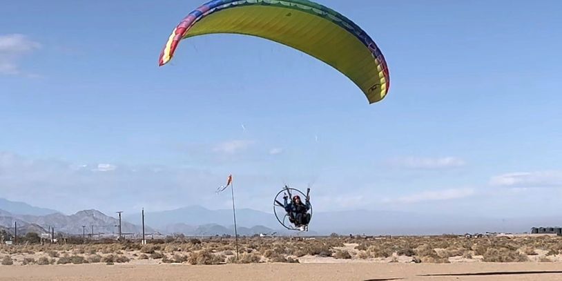 Person flying a powered paraglider over a desert landscape with mountains.